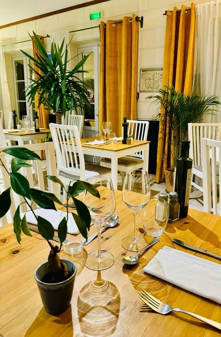 A dining table set with wine glasses, cutlery, and a napkin, surrounded by white chairs and potted plants.