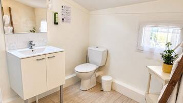 A bathroom with a white sink, toilet, and bidet, wooden flooring, and a window with a plant.