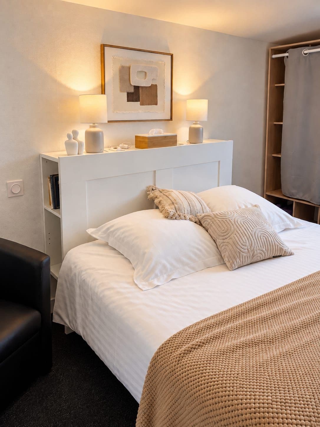 A hotel room with a bed, bedside tables, a lamp, a framed artwork, and a wardrobe.