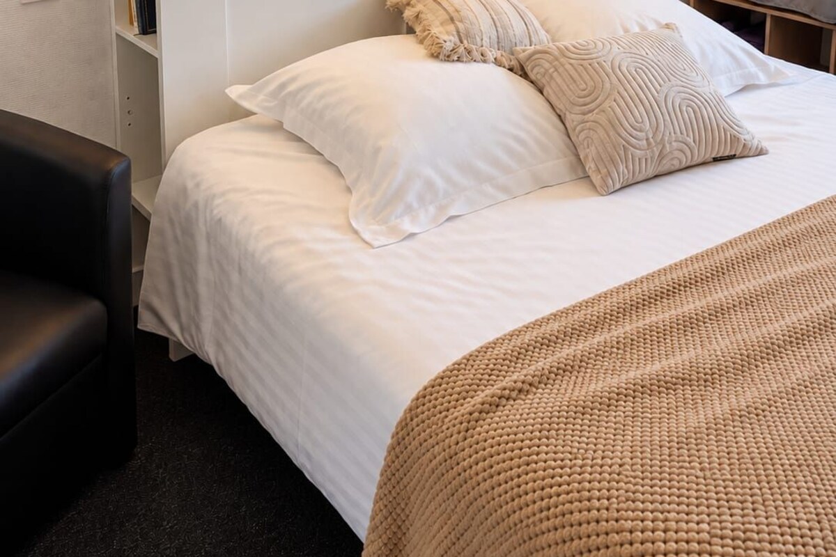 A hotel room with a bed, bedside tables, a lamp, a framed artwork, and a wardrobe.