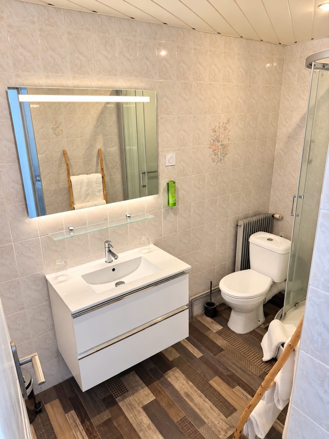 Un baño moderno con cabina de ducha de vidrio, un lavabo blanco con espejo sobre él y un inodoro con radiador en la parte de atrás.