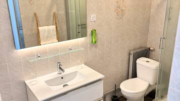Un baño moderno con cabina de ducha de vidrio, un lavabo blanco con espejo sobre él y un inodoro con radiador en la parte de atrás.