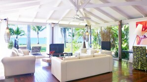A spacious living room with a large white sofa, a television, and a view of the ocean through large windows. - Villa Diosa del Mar (Veintisiete de Abril)
