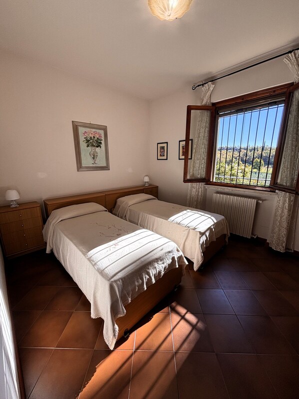 Une chambre avec deux lits, une table de chevet, une commode, une fenêtre donnant sur un beau paysage et un tableau encadré au mur.