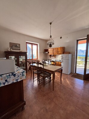 A kitchen with wooden cabinets, a dining table with chairs, a refrigerator, and a window with curtains.