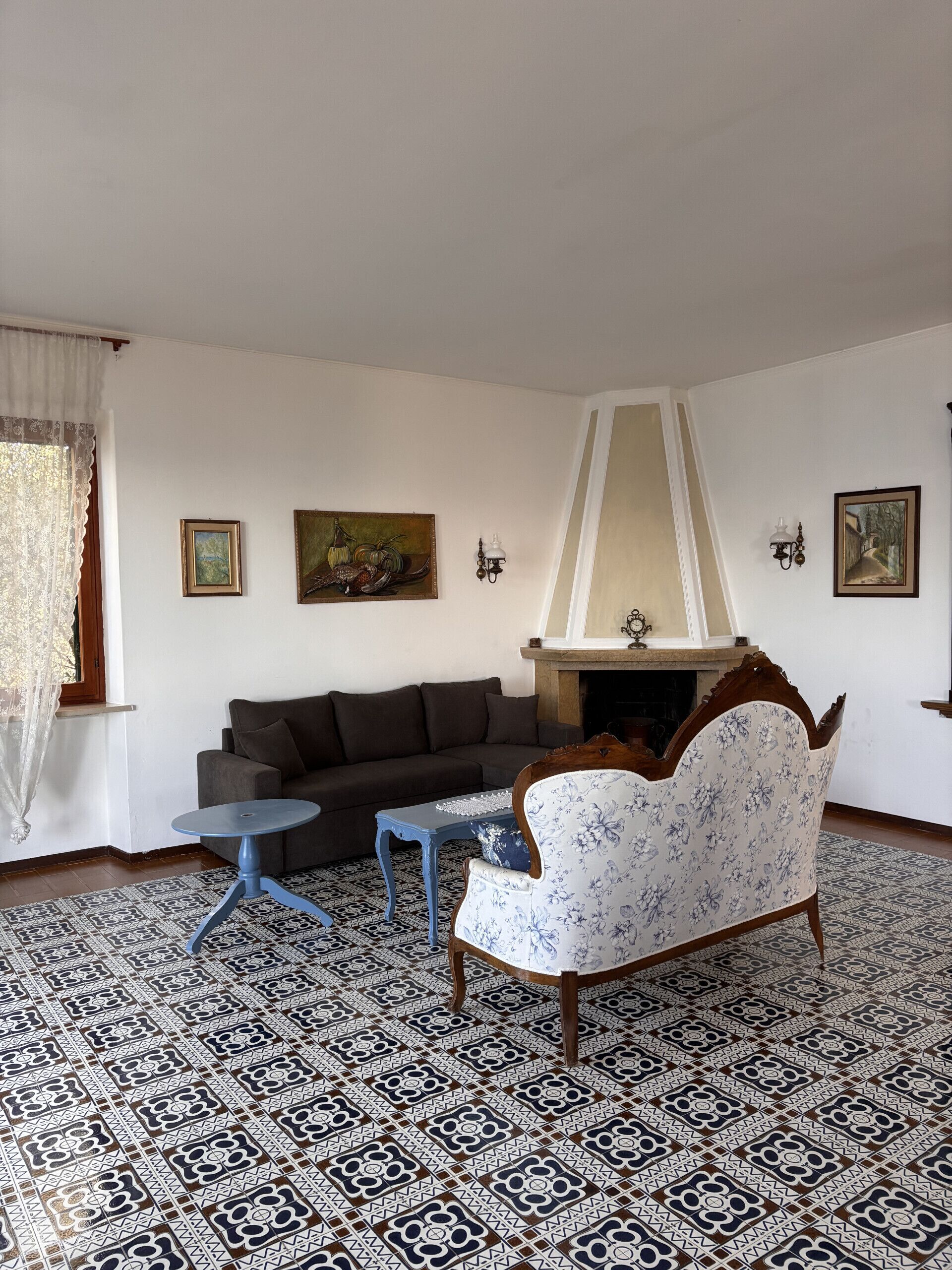 Una sala de estar con piso estampado, un sofá, un sillón floral, una mesita y una chimenea.