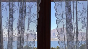 A view through a lace-curtained door to a balcony with a wooden floor and a metal railing, overlooking a mountainous landscape. - Villa Patrizia (Torri del Benaco)