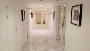 A corridor with white walls, framed pictures, and a glass door.