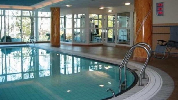 An indoor swimming pool with clear glass walls, metal railings, and a tiled floor.