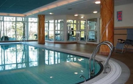 An indoor swimming pool with clear glass walls, metal railings, and a tiled floor.