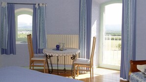 Un dormitorio con una cama, una mesa redonda con sillas y vistas amplias a través de ventanas grandes.