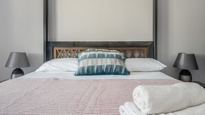 Ein ordentlich bezogenes Bett mit einer gestreiften Decke, einem geometrischen Kissen und zwei Nachttischlampen.