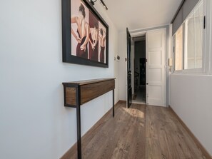 A hallway with a wooden floor, a framed artwork on the wall, and a door leading to another room.