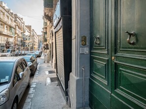 A narrow street lined with parked cars and buildings with green doors.
