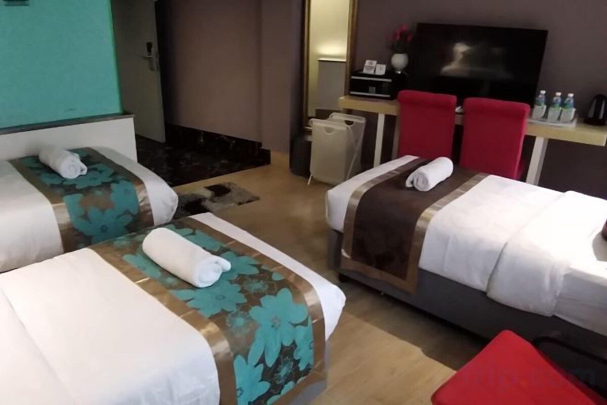 A hotel room with two beds, a TV, a desk with a chair, and a red couch.
