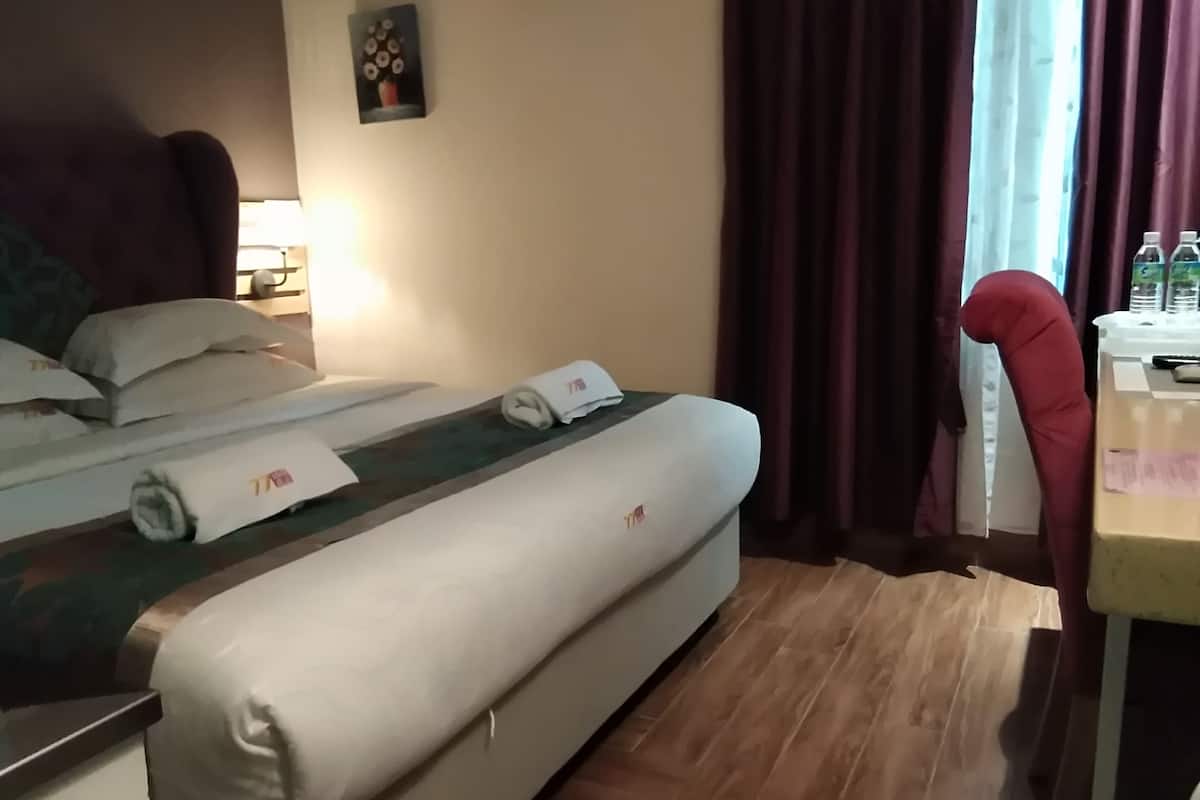 Ett hotellrum med en säng, ett skrivbord och en stol. Det finns kuddar och en hoprullad handduk på sängen. En tavla hänger på väggen.