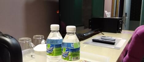 A hotel desk with two bottles of water, a glass jar, a white cup, and some packets on a tray.