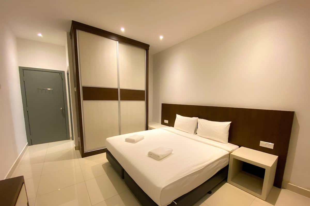 Habitación de hotel ordenada con una cama grande, una mesita de noche, un armario y una puerta.
