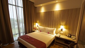 A hotel room with a large bed, wooden panel walls, two bedside lamps, a nightstand, a desk, a chair, and a window with curtains. - AZ Hotel & Serviced Apartments (Labuan)