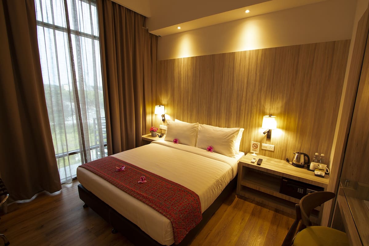 Habitación de hotel con una cama grande, paneles de madera, dos lámparas de noche, una mesita de noche, un escritorio, una silla y una ventana con cortinas.