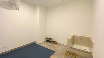 Une petite pièce propre, avec un tapis bleu, un lavabo blanc et un ventilateur au plafond.