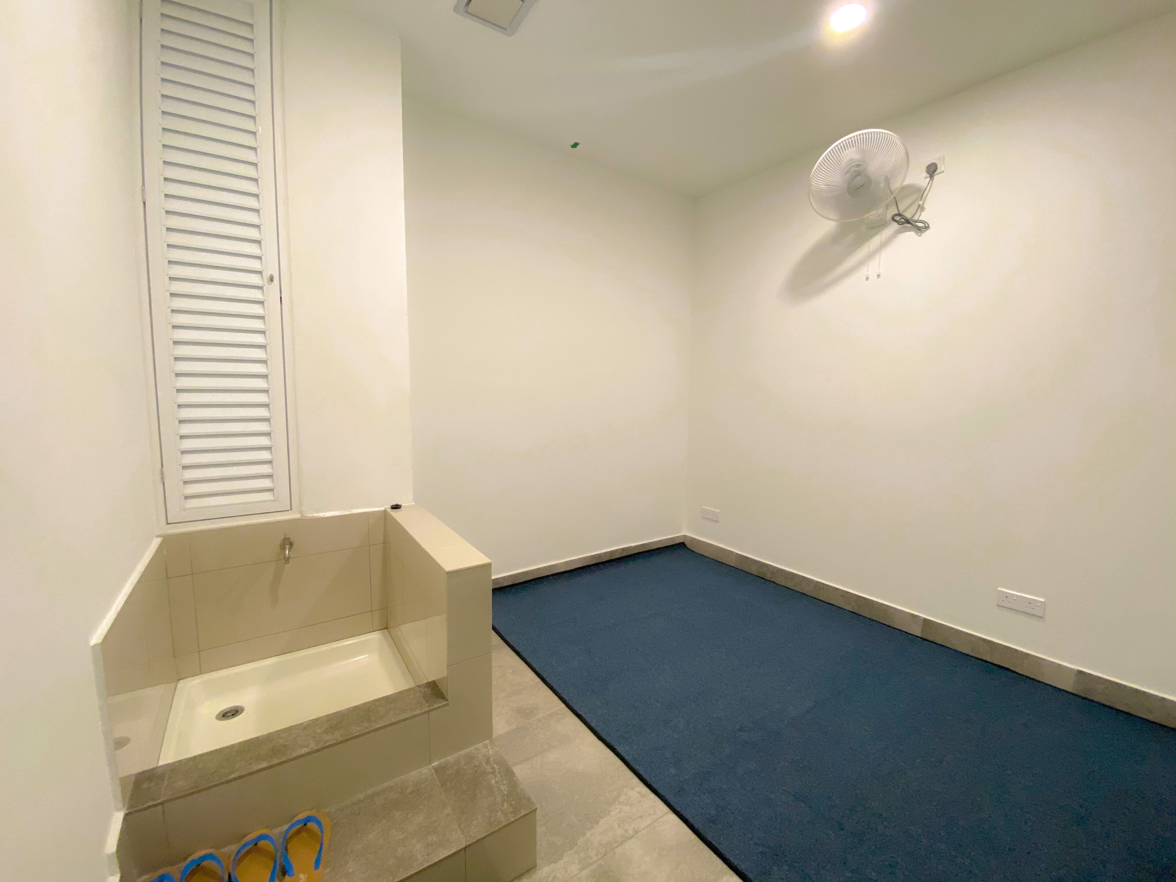 A room with a bathtub, a blue carpet, and a wall-mounted fan.