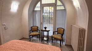 Ein Schlafzimmer mit einem großen Bett, zwei Sesseln, einem kleinen Tisch und einem Fenster mit Jalousien.