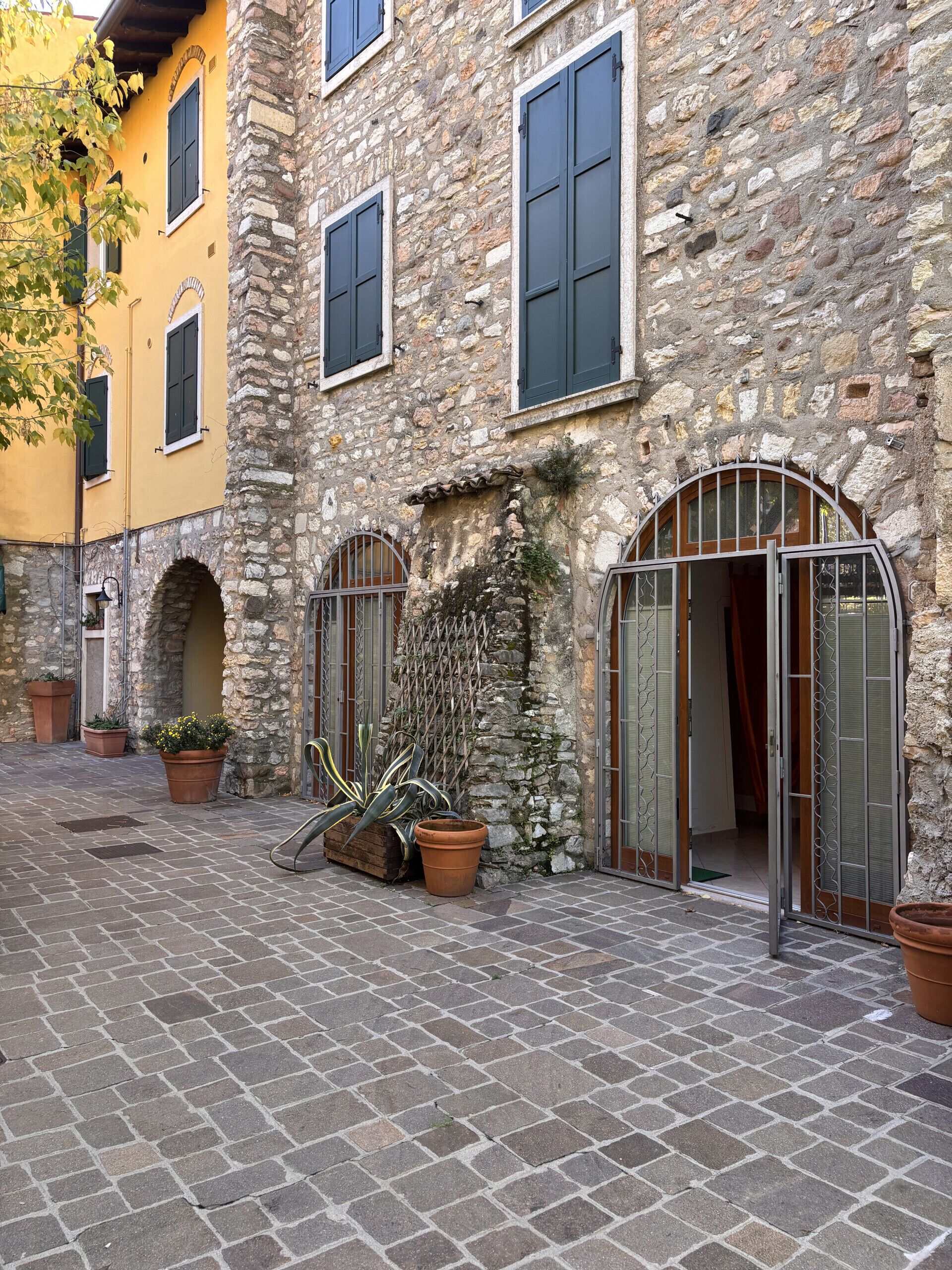 A stone building with arched windows and a door with metal bars. There are potted plants in front of the building.