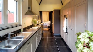 A modern kitchen with a long countertop, a built-in oven, and a window with curtains. - 't Aards Paradijs (Deinze)