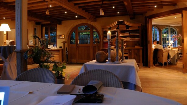 A cozy restaurant with wooden beams, tables set for dining, and a view through arched windows. - 't Aards Paradijs (Deinze)