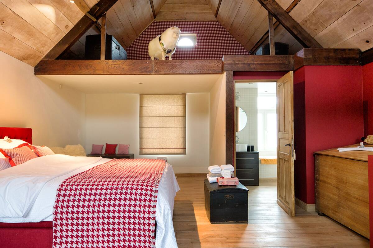 A loft bedroom with a sloped ceiling, a bed with a red and white checkered bedspread, a wooden bench, and a small window.