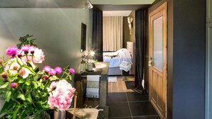 A hotel hallway with a bed, a sink, and a mirror. There are flowers on the left and a door on the right. - 't Aards Paradijs (Deinze)