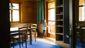 Ein Holzhütten-Interieur mit Essbereich, einem Kind in der Nähe eines Fensters und Regalen mit Geschirr.