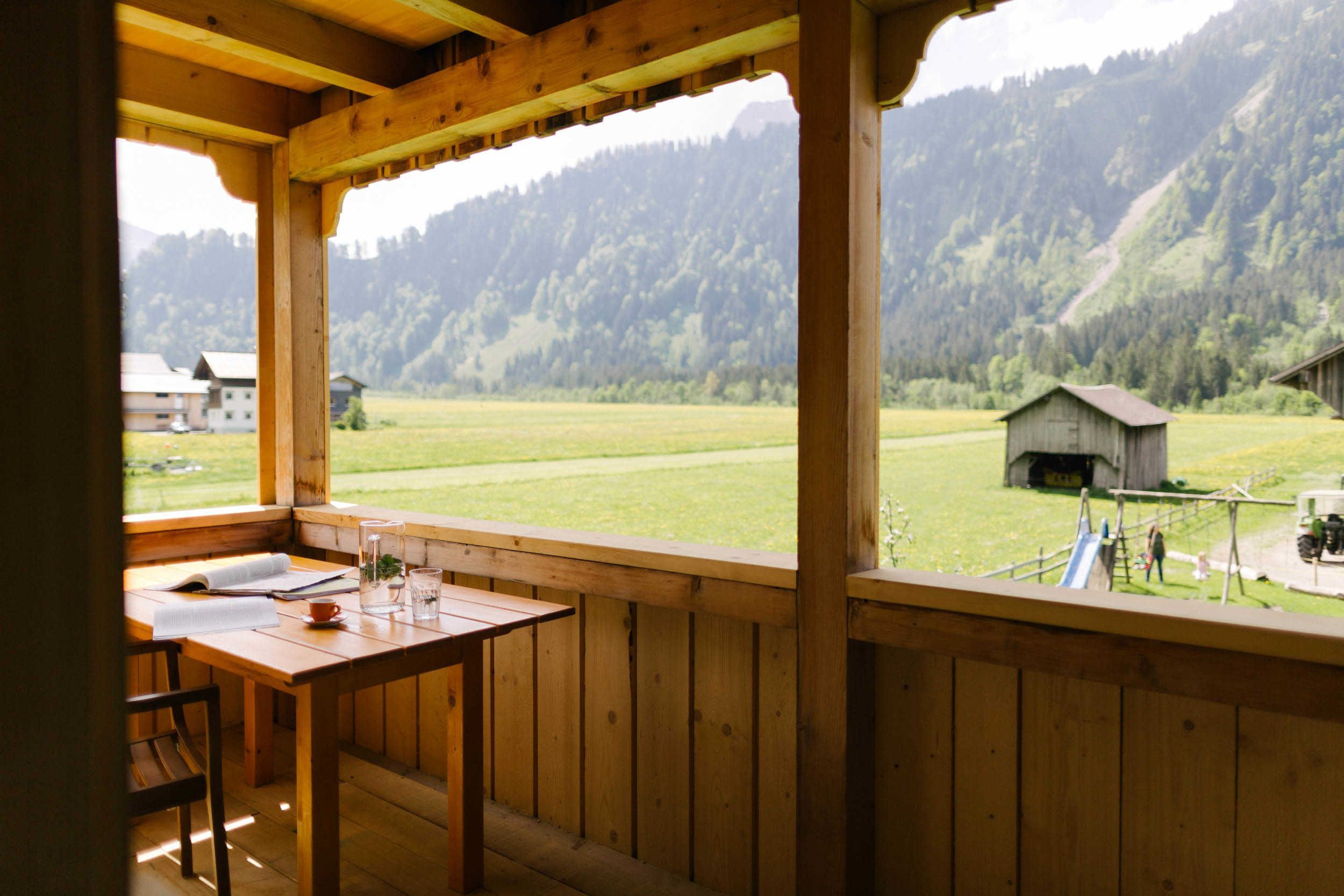 Een houten balkon met een tafel en stoelen, met uitzicht op een groen veld en een berg.