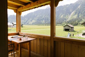 Un balcón de madera con una mesa y sillas, con vistas a un campo verde y una montaña.