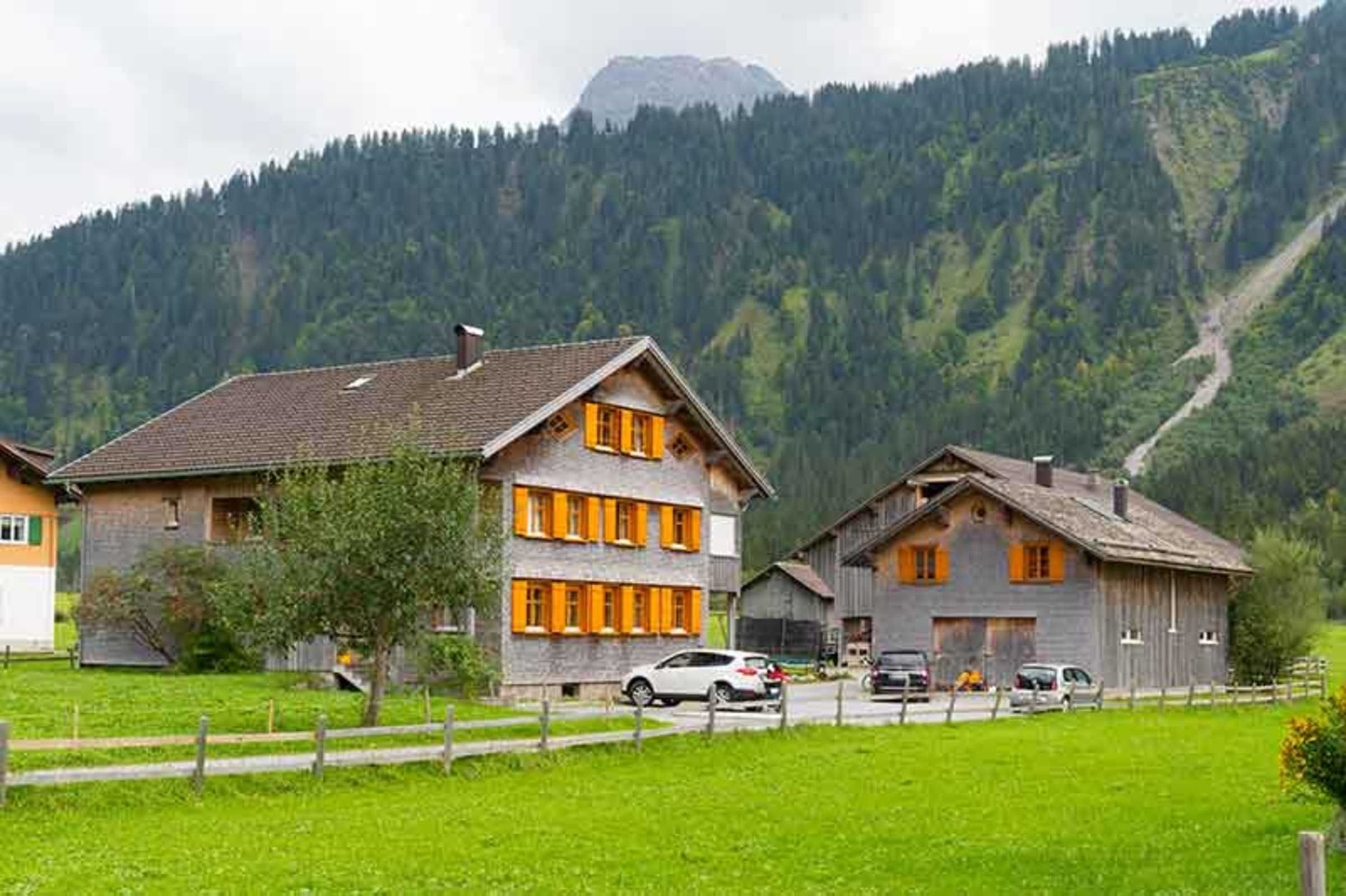 A rural setting with two wooden houses, one with a sloped roof and orange shutters, and another with a gabled roof.