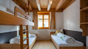 Ein Zimmer mit Etagenbetten, einem Vorhangfenster, einem Heizkörper und Holzbalken an der Decke.