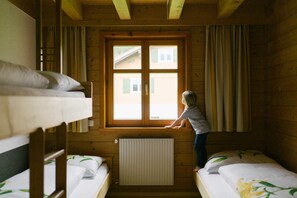 Habitación tipo cabaña de madera con literas, ventana con cortinas y radiador.