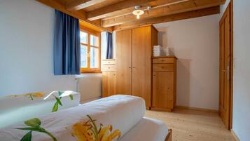 A bedroom with wooden beams, a window with curtains, a radiator, and a wardrobe.