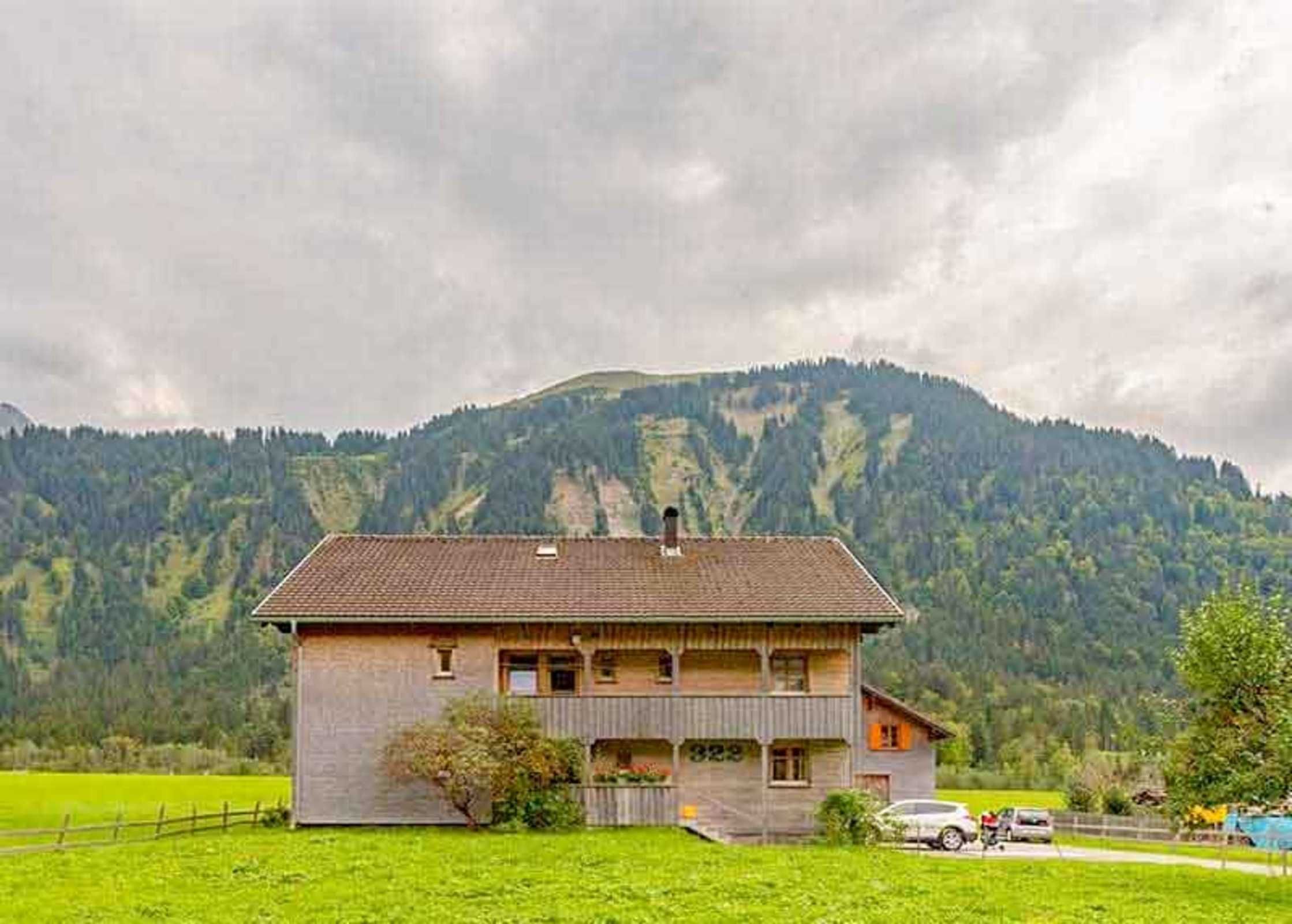Una casa a due piani in legno con un balcone, con montagne sullo sfondo.