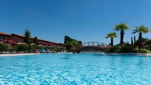 A swimming pool with a bridge, palm trees, and a building with red awnings.