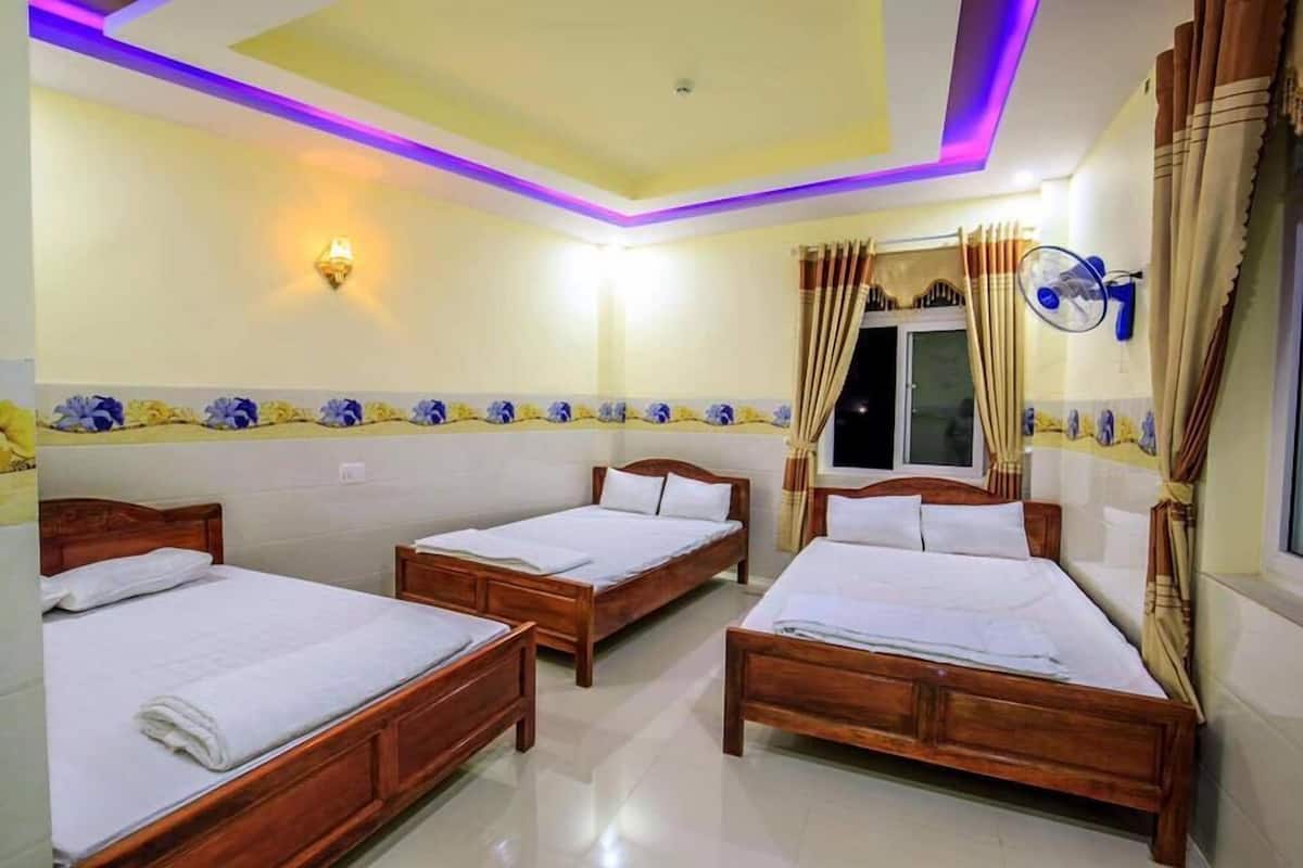 Habitación de hotel con tres camas de madera, techo con iluminación LED púrpura, televisor montado en la pared y cortinas.