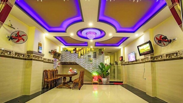 A hotel lobby with a polished floor, a staircase, and a dining area with wooden chairs and a table. - Dinh Sa Ly Son Hotel (Ly Son)