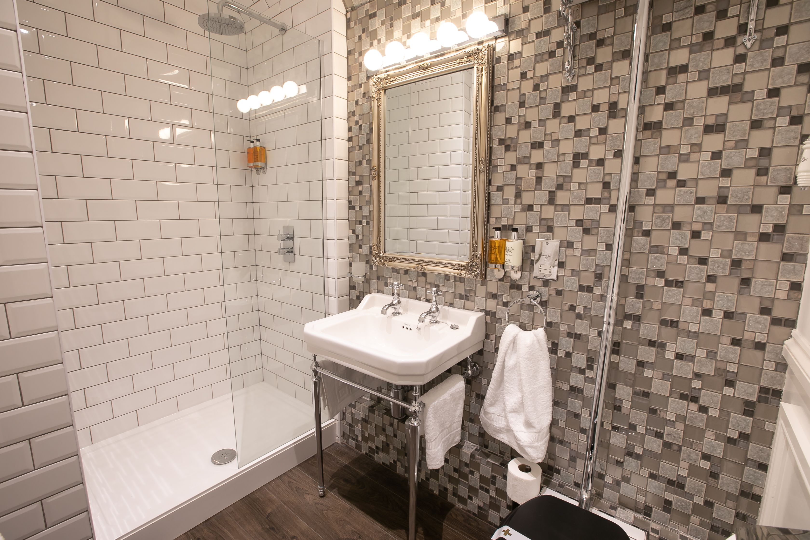 A modern bathroom with a white sink, a glass-enclosed shower, and a mosaic-patterned wall.