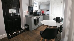 A compact kitchen with modern appliances, a dining area with a round table, and a black door with a notice. - Number 82 The Unthank (Norwich)