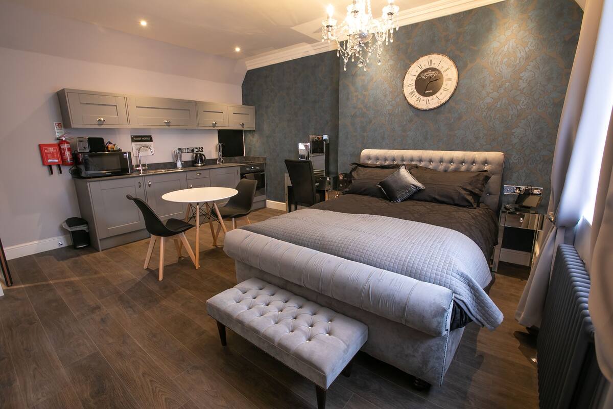 Un dormitorio moderno con una cama grande, un escritorio pequeño y una kitchenette.