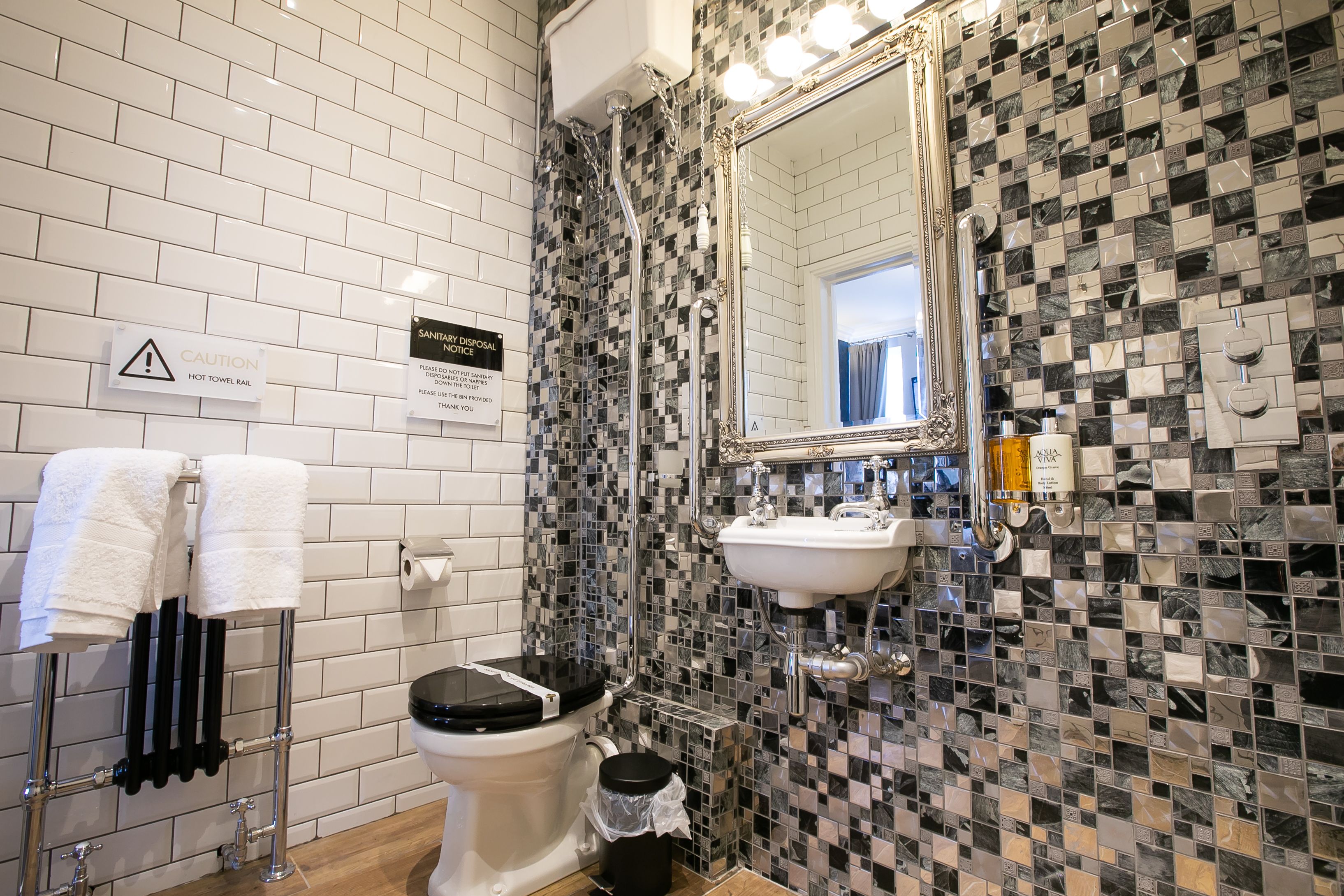 A bathroom with a tiled wall, a sink, a toilet, and a towel rack.
