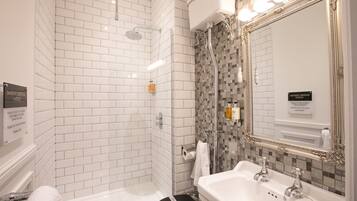 Un bagno con pareti piastrellate di bianco, una doccia con porta in vetro, un lavandino con due rubinetti e uno specchio con cornice decorata.