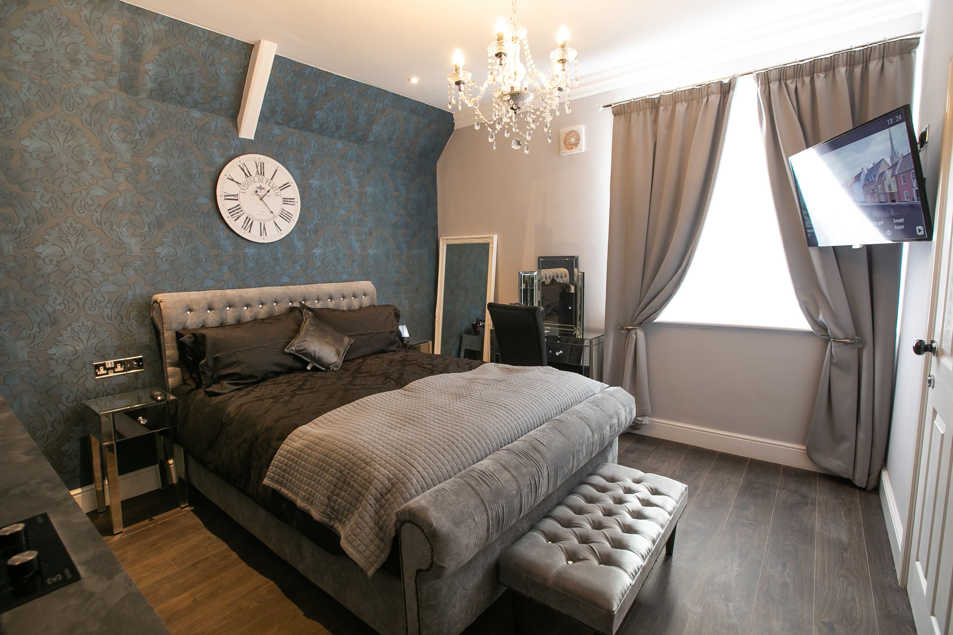 A bedroom with a large bed, a bedside table, a TV, and a chandelier.