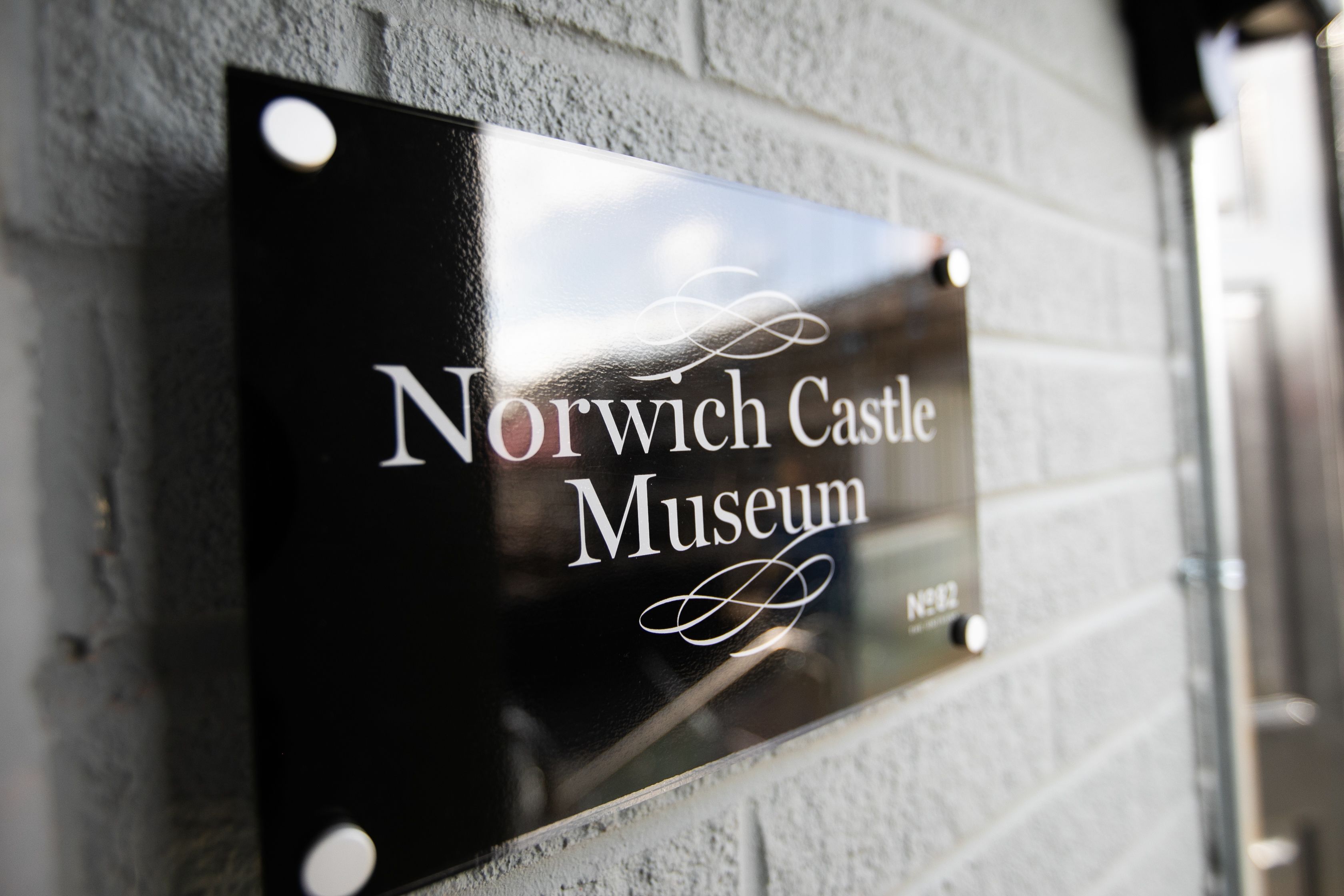 A sign for the Norwich Castle Museum mounted on a brick wall.